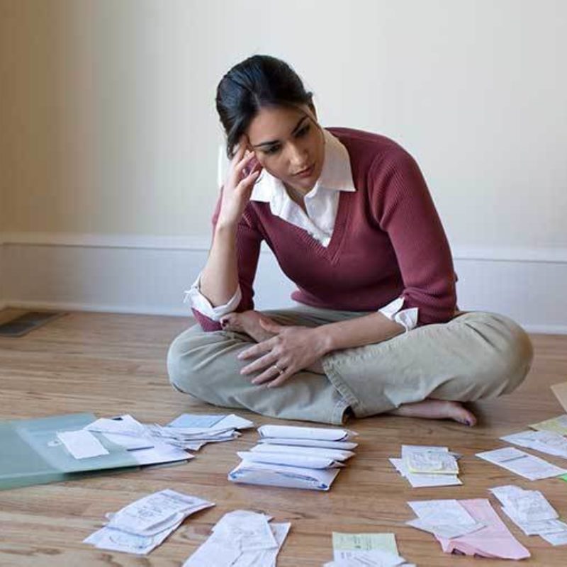 Contemplitive woman reviews papers while sitting on a wooden floor.
